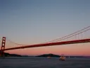 De Golden Gate Bridge bij zonsondergang met een zeilboot en enkele andere boten op het water.