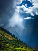 Zonnestralen die door wolken breken boven een berglandschap met groene terrasvelden.