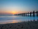 Zonsondergang boven zee met een rij houten palen die het strand in de zee in leiden.