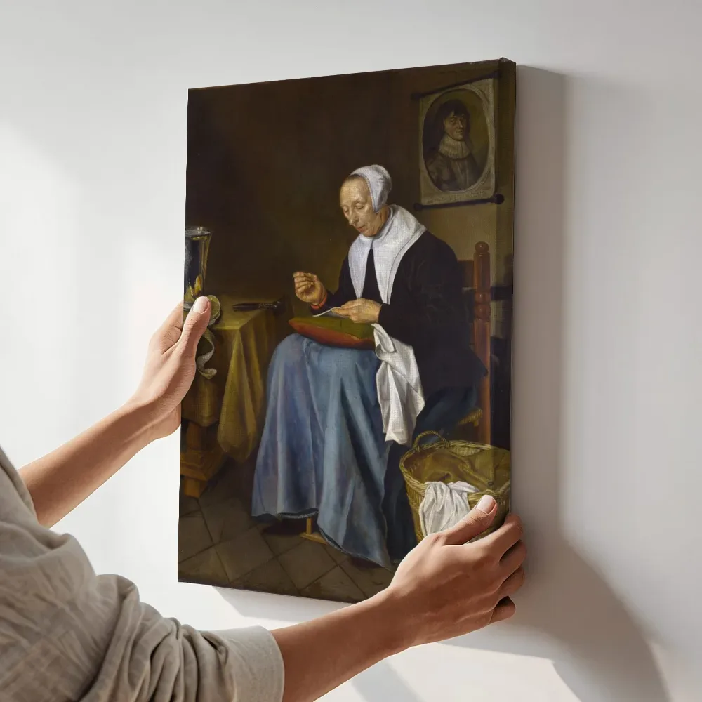 Sfeerimpressie: Oude vrouw, zittend te naaien van Johannes van der Aeck terwijl het aan de muur wordt gehangen